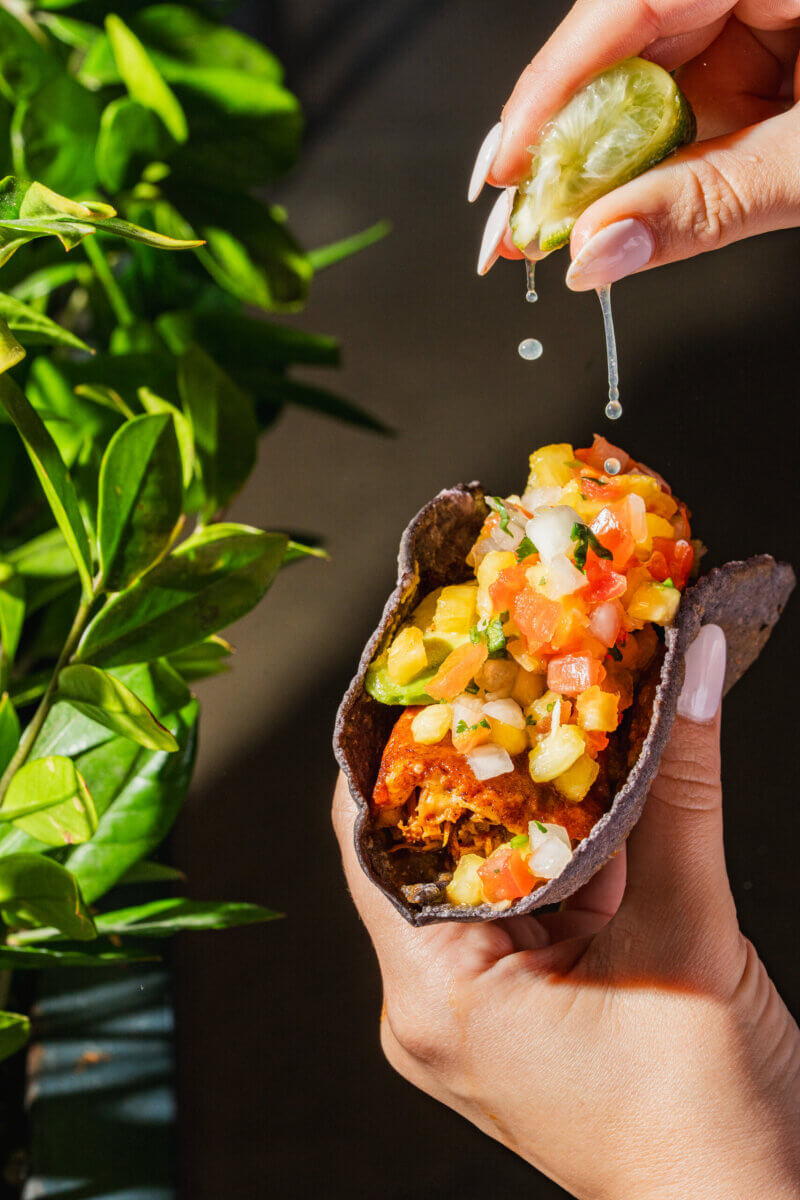 12 New Nashville Restaurants to Try This Month - 10 Hand squeezing lime over a taco filled with diced vegetables and salsa, held above a dark surface next to a green plant—capturing the fresh flavors and vibrant energy of new restaurants appearing in September across Nashville’s lively dining scene.
