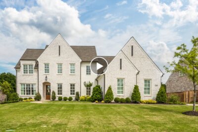 Large white brick house with steep gable roofs sits on a green lawn with shrubs, under a partly cloudy sky overhead. Located at 1548 Paso Fino Trail in Collierville, TN, this charming residence offers timeless curb appeal and a welcoming atmosphere.