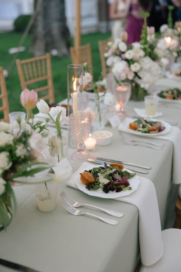 A Nashville Bride's Beautiful Tribute to Her Late Dad Only Made the Wedding More Joyful - 16 Elegant outdoor dining table set for a garden-party wedding at Brentwood’s Ravenswood Mansion, with plates of salad, candles, pink glassware, and floral centerpieces on a light green tablecloth.