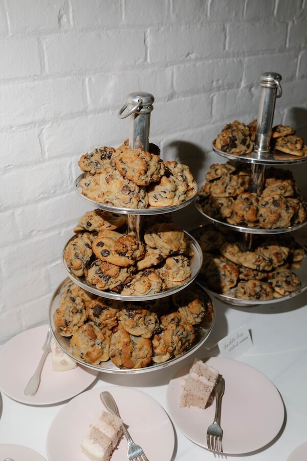 A Nashville Bride's Beautiful Tribute to Her Late Dad Only Made the Wedding More Joyful - 17 Two tiered trays filled with chocolate chip cookies on a white table at a charming Garden-Party Wedding, with plates of sliced cake and forks in the foreground—perfect for celebrating at Ravenswood Mansion in Brentwood.