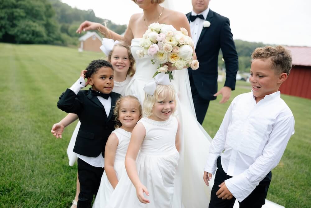 A Nashville Bride's Beautiful Tribute to Her Late Dad Only Made the Wedding More Joyful - 10 A bride holding a bouquet stands outside with four children in formal attire and a man in a suit on the grassy lawn at Ravenswood Mansion, capturing the charm of a Brentwood garden-party wedding.