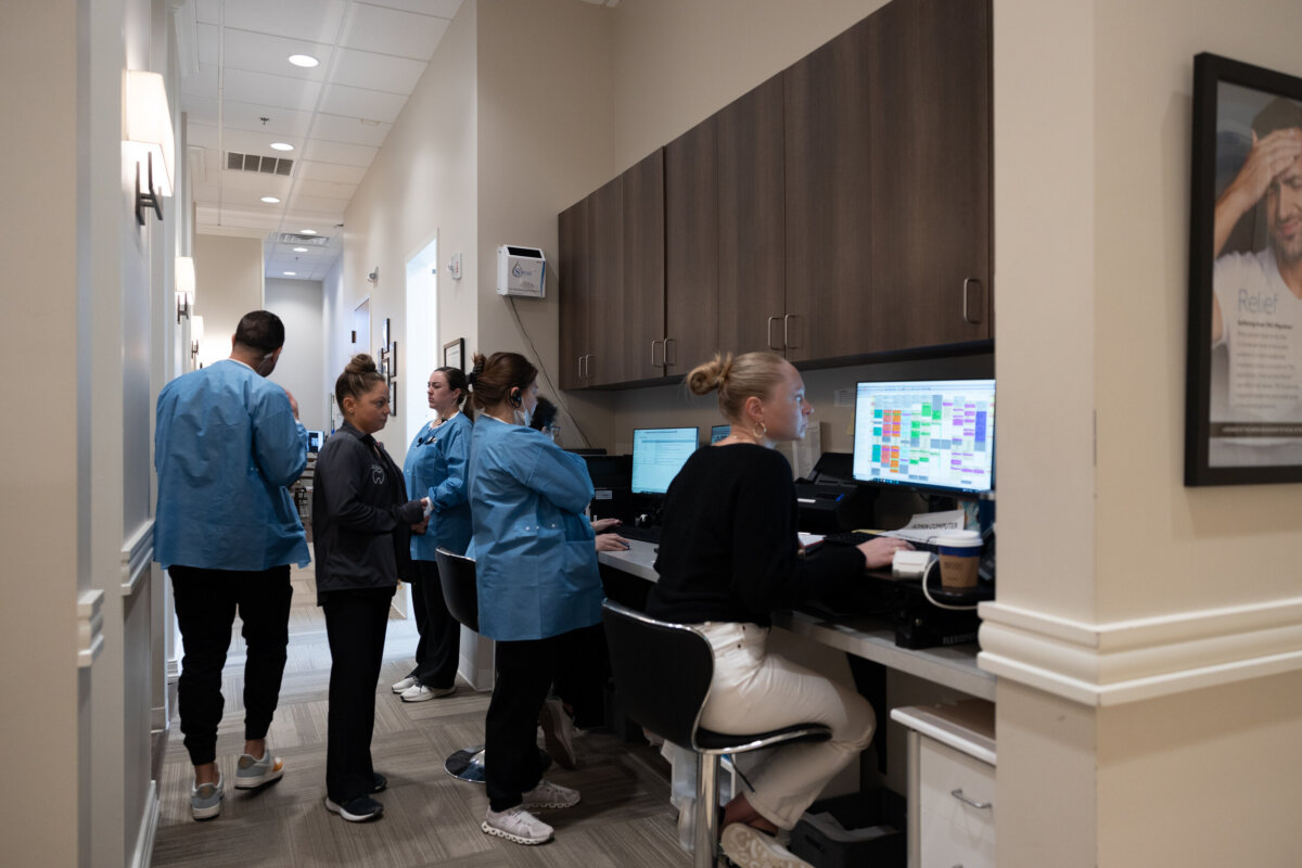 Healthy Smiles for Life: A Guide to Family Dental Care For Every Age - 7 Several healthcare workers in blue scrubs and a woman at a computer work in a medical office hallway with beige walls and wood cabinets, creating an inviting atmosphere for family dental care and healthy smiles.
