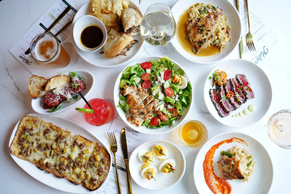 The Best Culinary Hot Spots in the South - 7 A table set with various dishes—including salad, steak, flatbread, deviled eggs, sandwiches, drinks, and dessert—arranged on white plates and glasses evokes the inviting charm of the South’s best restaurants and culinary hot spots.
