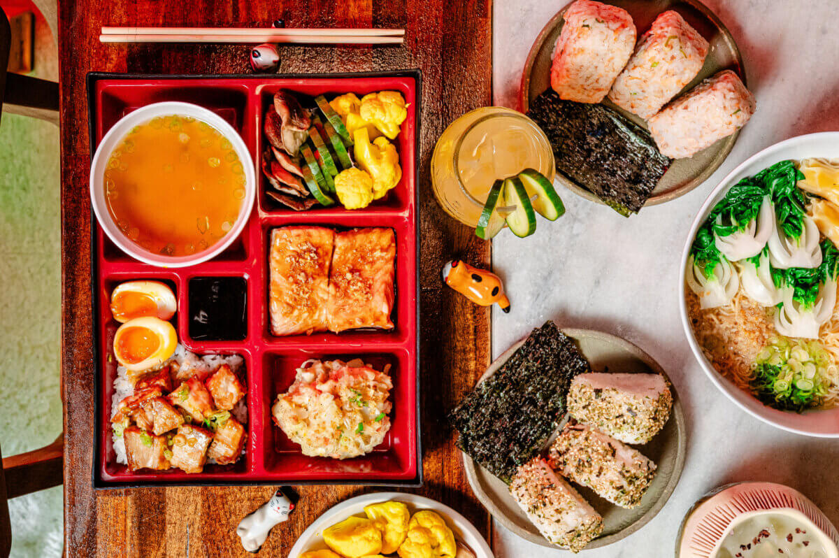 The Best Culinary Hot Spots in the South - 2 A bento box with rice, soup, eggs, tofu, and vegetables sits on a table with sushi, noodles, pickles, seaweed, and a glass of drink—an arrangement reminiscent of the creative presentations found at some of the best southern restaurants—garnished with small animal figurines.