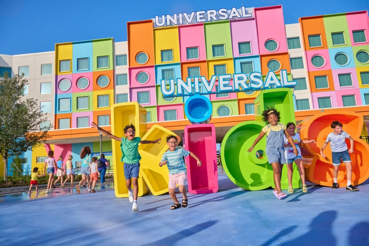 Children run and play in front of a colorful hotel entrance with large letters spelling “kids” and “Universal” on the building behind them, making it a perfect stop for families exploring Southern attractions on their travel road trip.