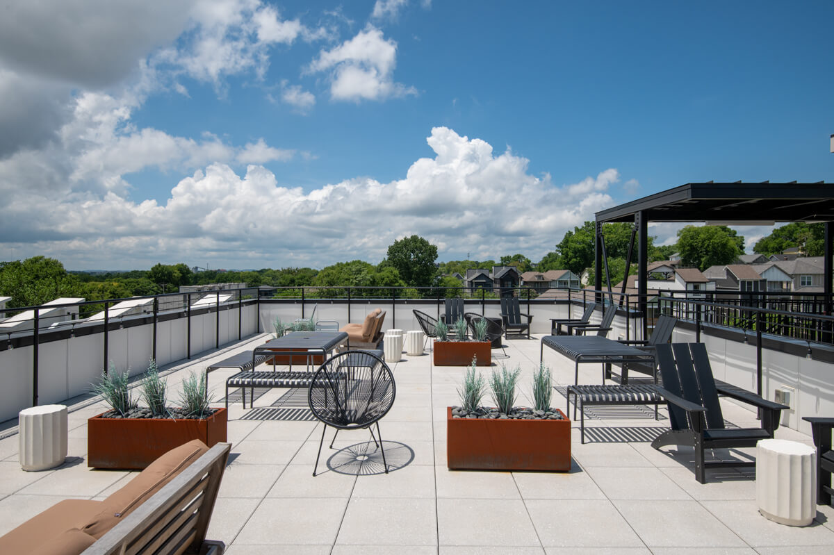 A rooftop patio at 1310 Lischey Ave in Nashville, TN, with outdoor seating, planters, and a pergola, overlooks trees and houses under a partly cloudy sky.