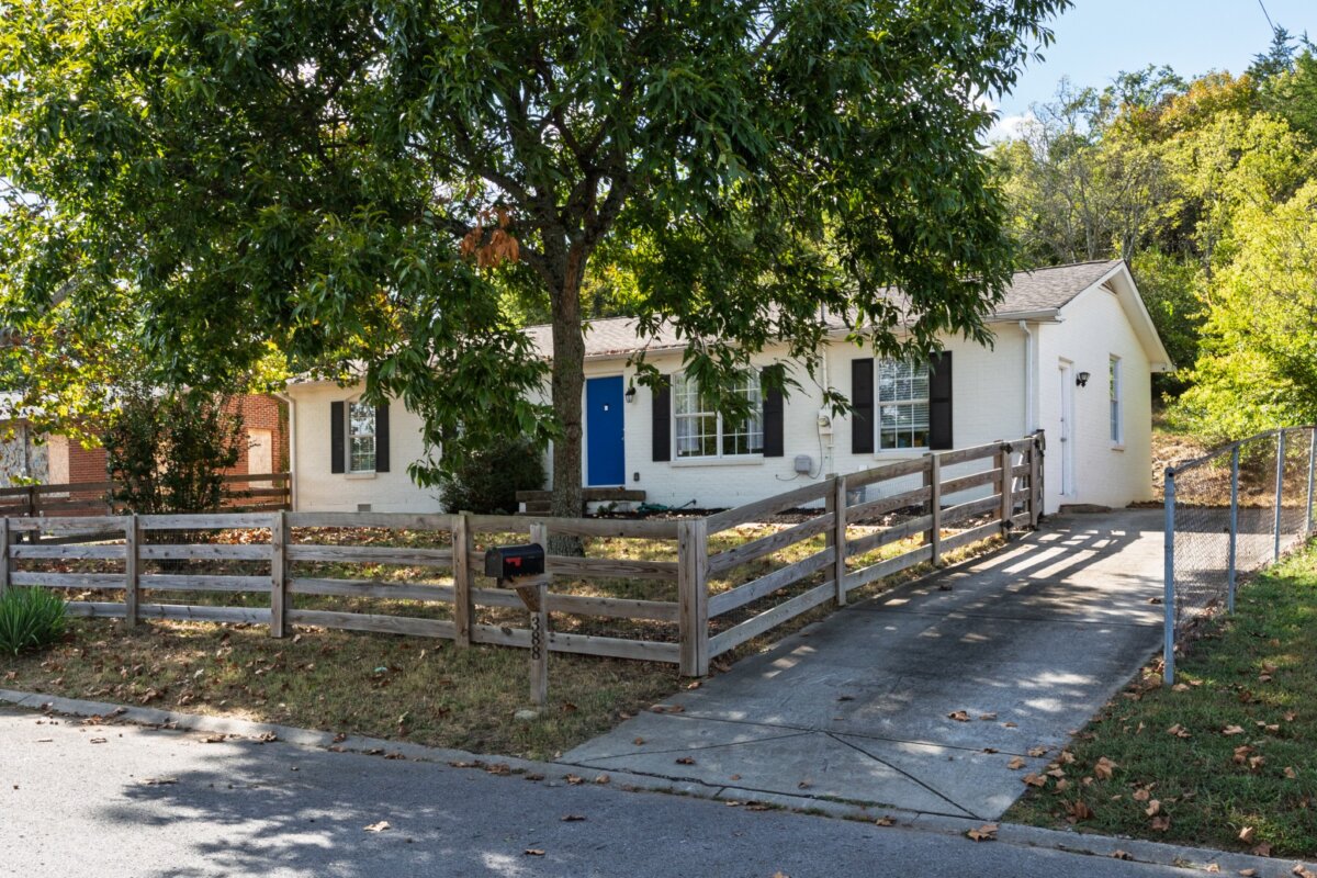 A white single-story Nashville home at 388 Kingview Dr featuring black shutters, a blue front door, and a wooden fence in the front yard.
