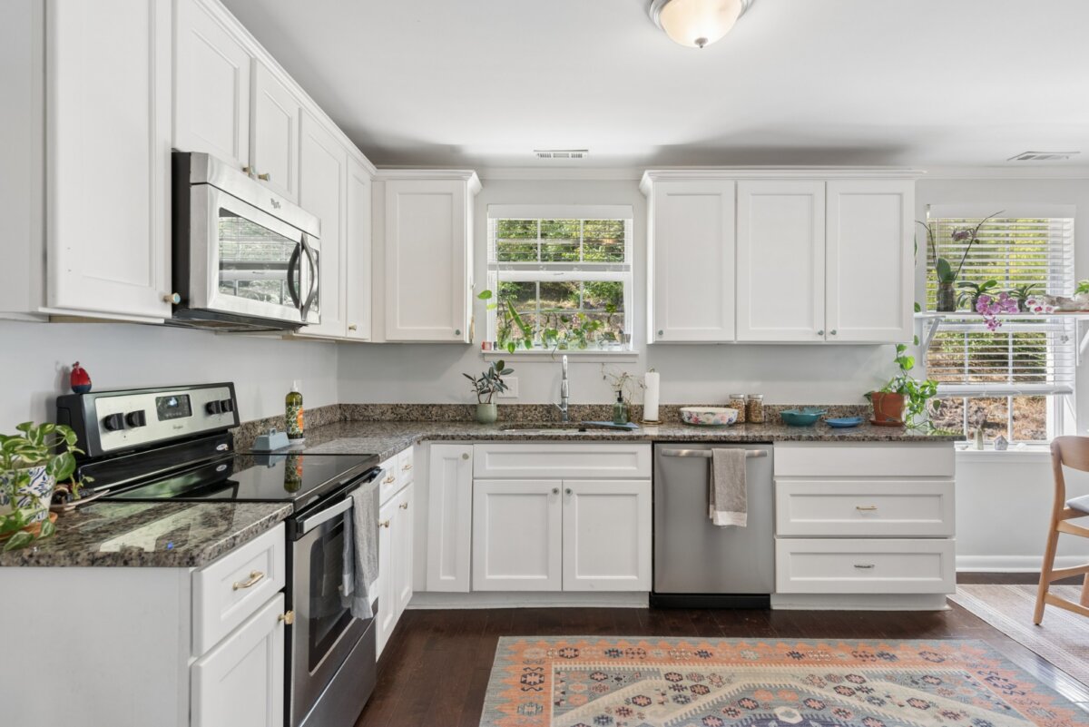 A kitchen in this Nashville home features white cabinets, speckled countertops, stainless steel appliances, and a patterned rug on a dark wood floor.