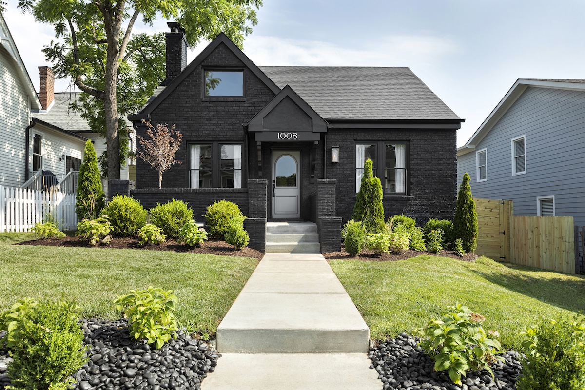 A single-story black brick house with white trim, an arched front door, and a concrete walkway leading to the entrance.