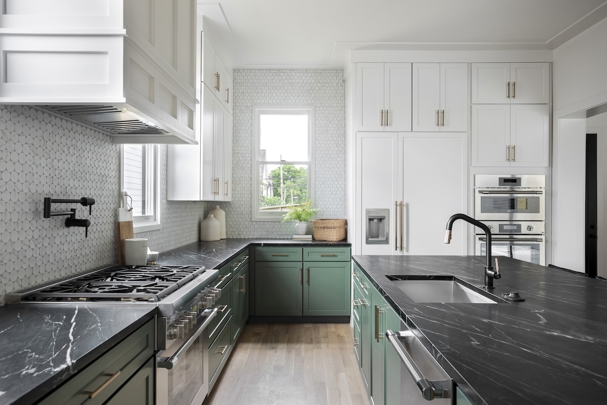 A kitchen with white upper cabinets, green lower cabinets, and black marble countertops.