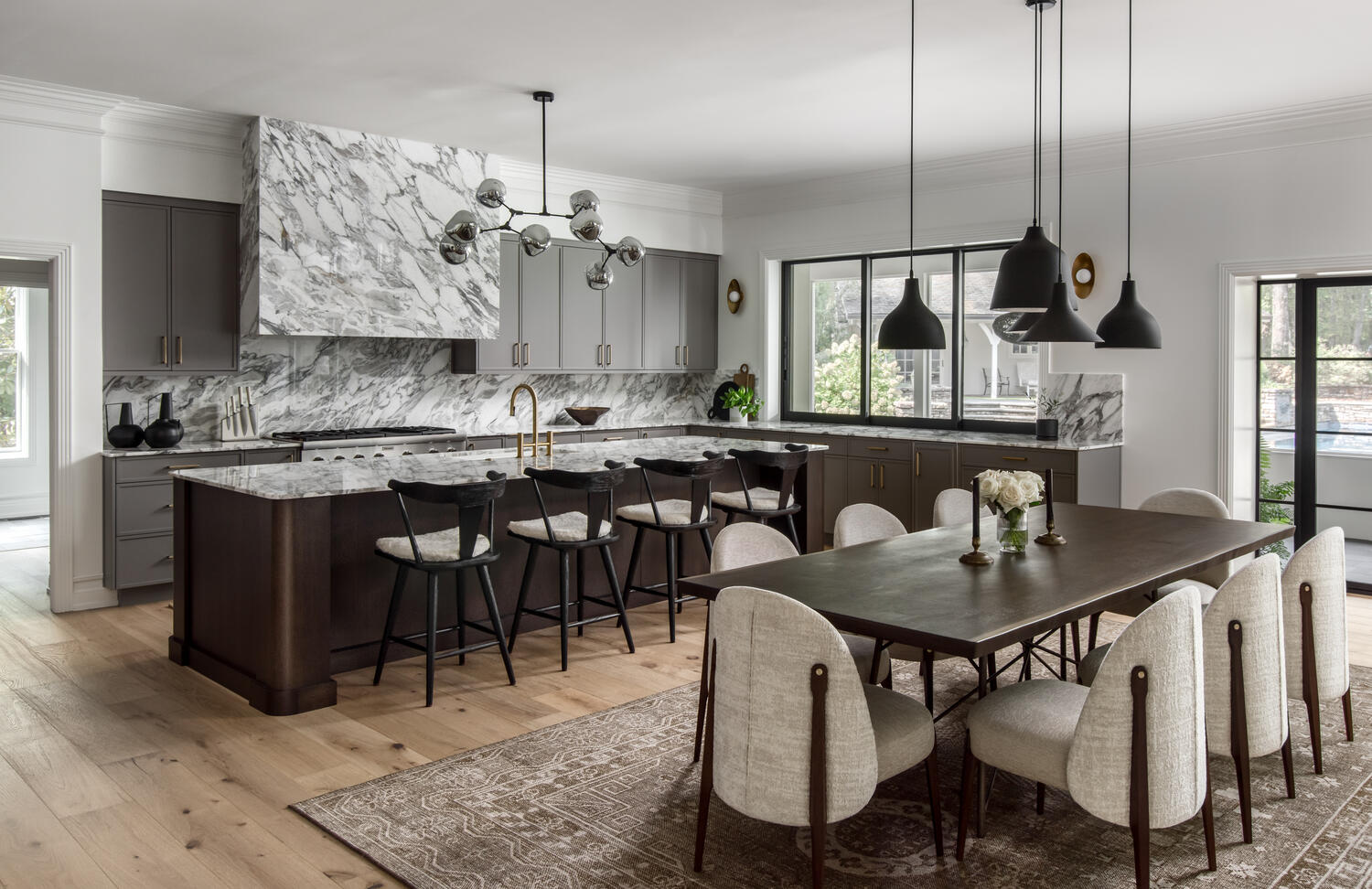 A kitchen with grey cabinets, a marble-topped island with stools, and a dining table with six upholstered chairs.