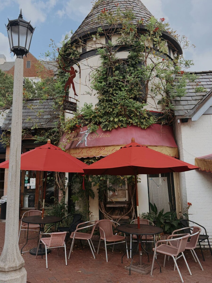 3 Cozy Fall Reads (Plus the Best Spots to Read Them in BHAM!) - 5 Outdoor patio with two red umbrellas and tables in front of an ivy-covered bakery, a perfect Birmingham reading spot.
