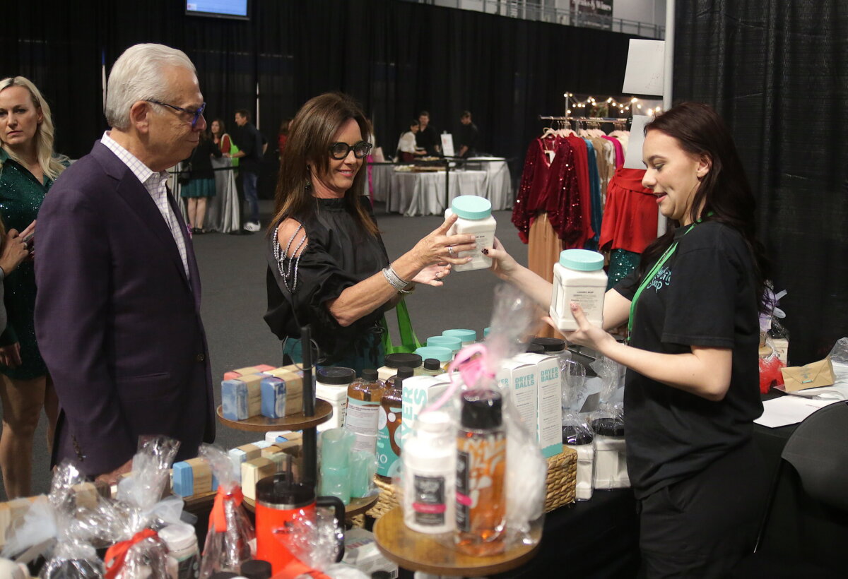 A woman in a black shirt hands a jar of laundry products to a customer at a Junior League of Birmingham vendor booth.