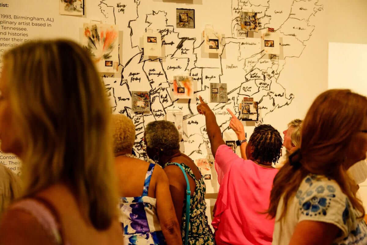 Your Guide to Birmingham's Historic 4th Avenue Historic District - 4 People look at an art installation featuring small framed works attached to a wall-sized map of the United States in the 4th Avenue District of Birmingham.