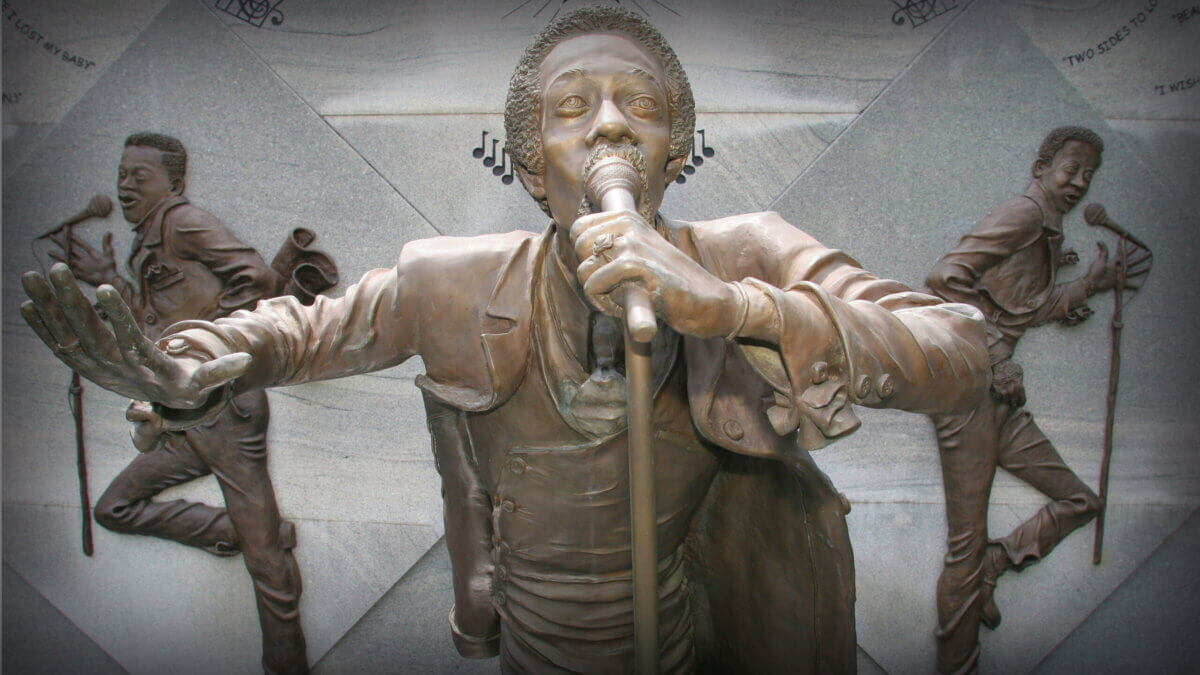 Your Guide to Birmingham's Historic 4th Avenue Historic District - 5 Bronze relief sculpture of The Temptations in the Birmingham 4th Avenue District, featuring a lead singer with a microphone flanked by two dancing figures against a stone background.