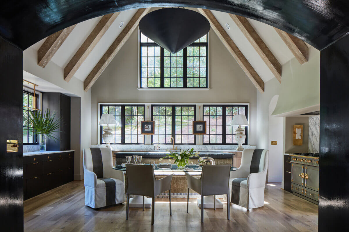 Your Home Should Tell Your Story — and Leigh Misso Wants to Help You Write It - 3 A dining area by River Brook Design features a glass-topped table and four chairs set before a kitchen counter under a vaulted ceiling with exposed wooden beams.