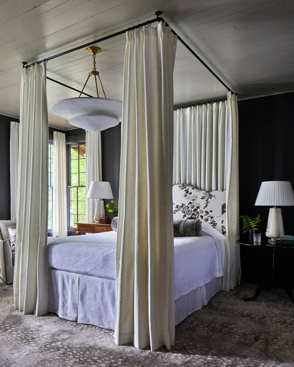 Your Home Should Tell Your Story — and Leigh Misso Wants to Help You Write It - 8 A River Brook Design and Construction four-poster bed with white curtains and a floral headboard stands in a bedroom with dark walls.