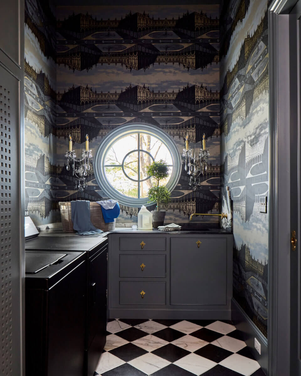 Your Home Should Tell Your Story — and Leigh Misso Wants to Help You Write It - 9 A laundry room by Leigh Misso featuring gray cabinets, a black countertop, a circular window, and architectural wallpaper above a black-and-white checkered floor in this River Brook Design project.