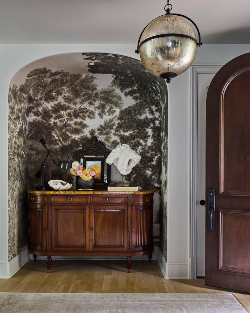 Your Home Should Tell Your Story — and Leigh Misso Wants to Help You Write It - 11 A wood sideboard with flowers, a lamp, and decorative objects sits in an arched alcove with landscape wallpaper in this River Brook Design architectural space.
