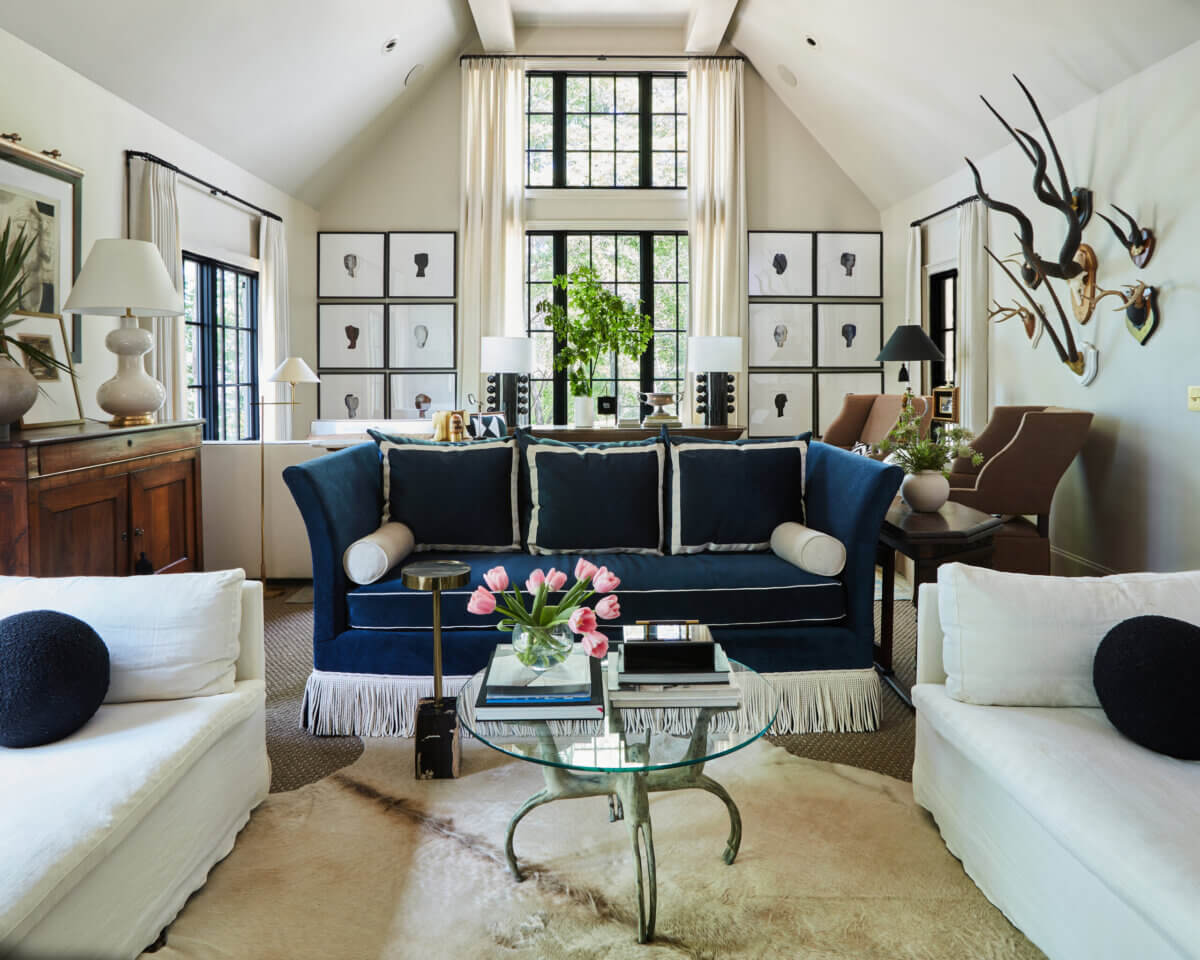 Your Home Should Tell Your Story — and Leigh Misso Wants to Help You Write It - 5 A living room by River Brook Design and Construction features a blue sofa, white armchairs, and a glass-topped coffee table with pink tulips under a vaulted ceiling with large windows.
