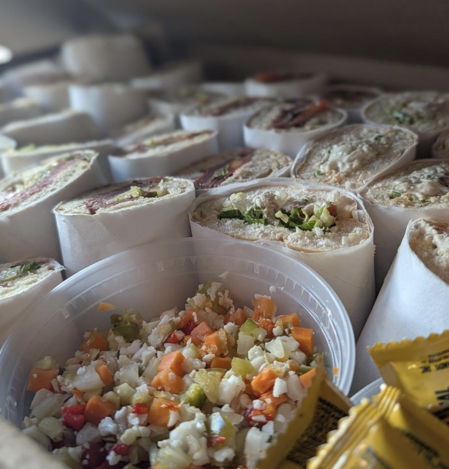 5 New Birmingham Restaurants to Try This Month (Plus An Expansion & A Relocation!) - 2 A container of chopped vegetable salad in the foreground, with many wrapped sandwich halves behind it.