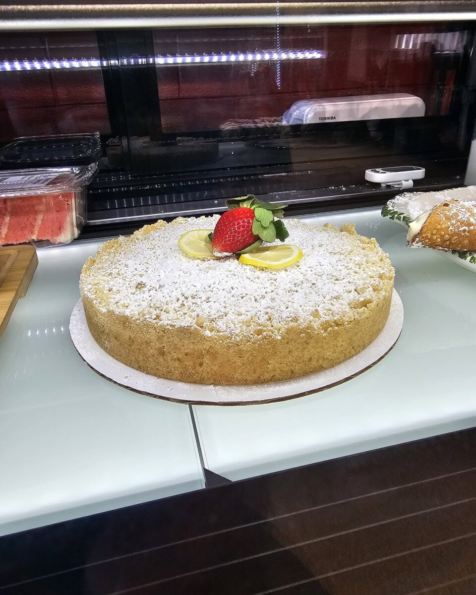 5 New Birmingham Restaurants to Try This Month (Plus An Expansion & A Relocation!) - 4 A round cake with a crumb topping, dusted with powdered sugar and garnished with two lemon slices and a strawberry.