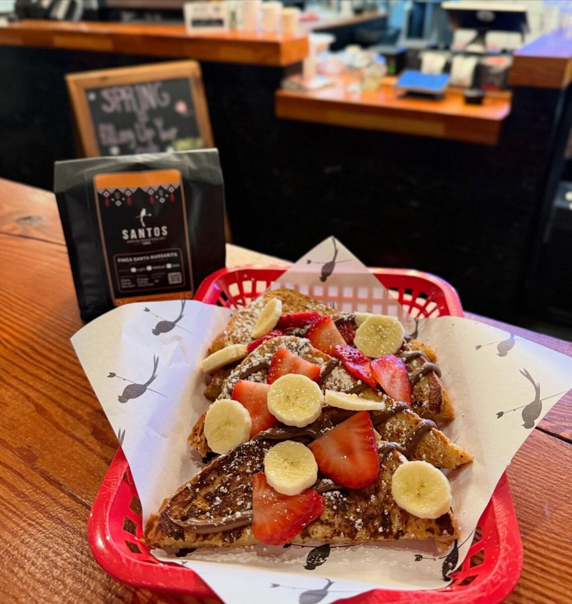 5 New Birmingham Restaurants to Try This Month (Plus An Expansion & A Relocation!) - 8 French toast topped with chocolate spread, strawberries, and banana slices in a red basket next to Santos coffee beans, a staple for Birmingham restaurants.