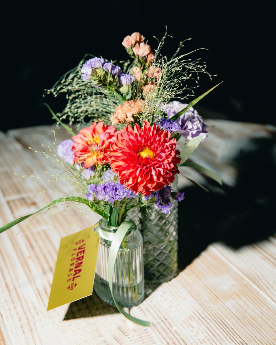 What Happens When You Bring 22 Birmingham Strangers Together and Say "Trust Me"? - 7 A bouquet of red dahlias and purple statice from Trust Me Night in two glass vases, with a yellow “Vernal Florals” tag tied to one.