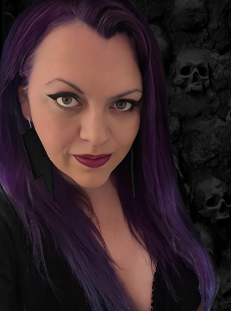 A woman with long purple hair and black lightning-bolt-shaped earrings.