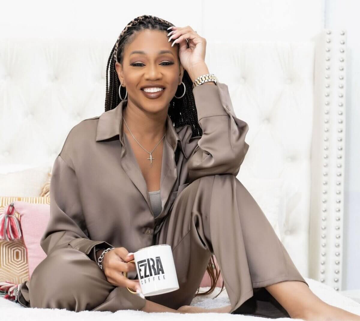 She Started Roasting Coffee on Her Stovetop. Now Target & Amazon Are Calling. - 2 Jessica Taylor sits on a bed, smiling in silky brown pajamas and holding a white mug with “EZRA COFFEE” printed on it.