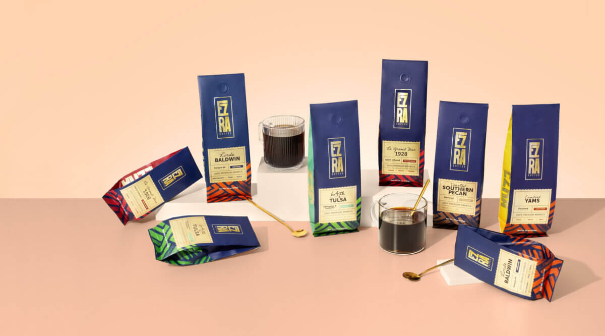 She Started Roasting Coffee on Her Stovetop. Now Target & Amazon Are Calling. - 4 Eight blue Ezra coffee bags, two green coffee bags, two glasses of black coffee, and two gold spoons are arranged on a pink and beige surface.