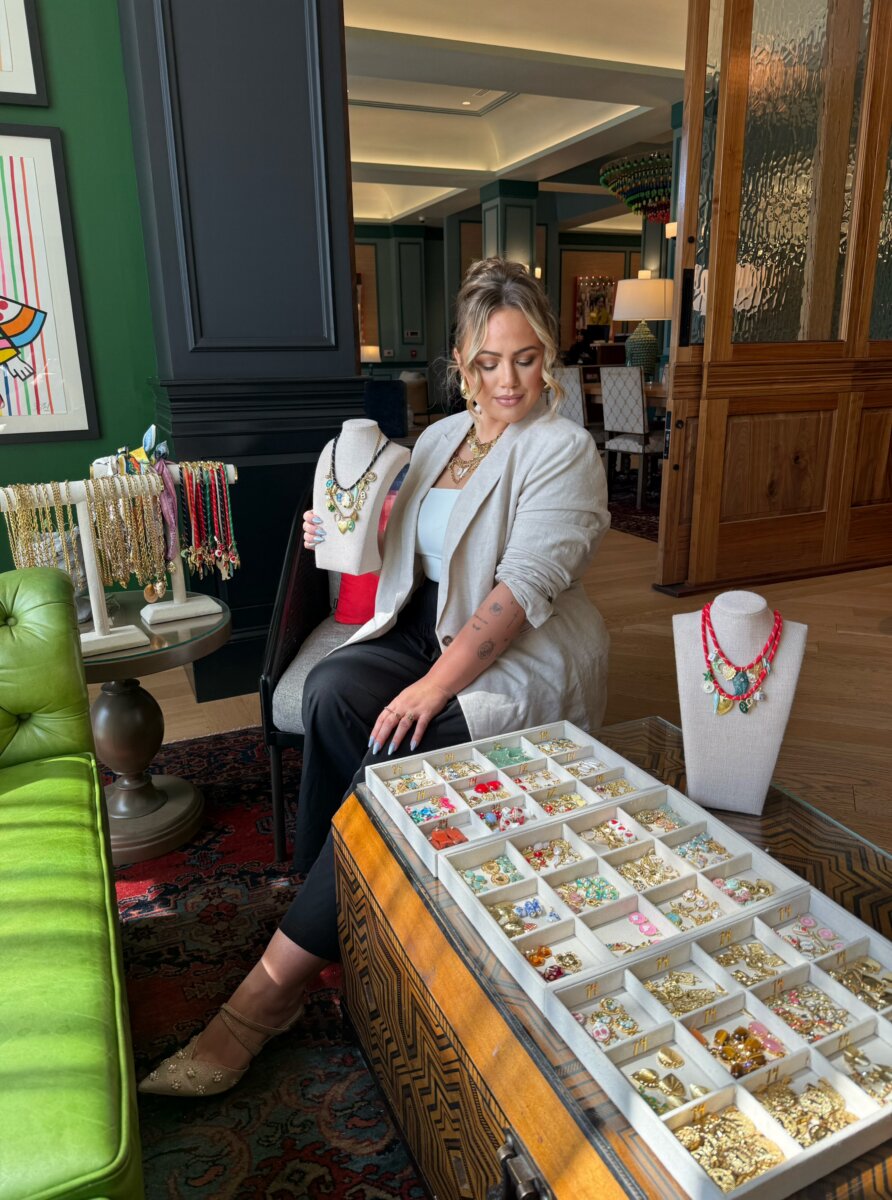 A woman sits with trays of charms and necklaces.