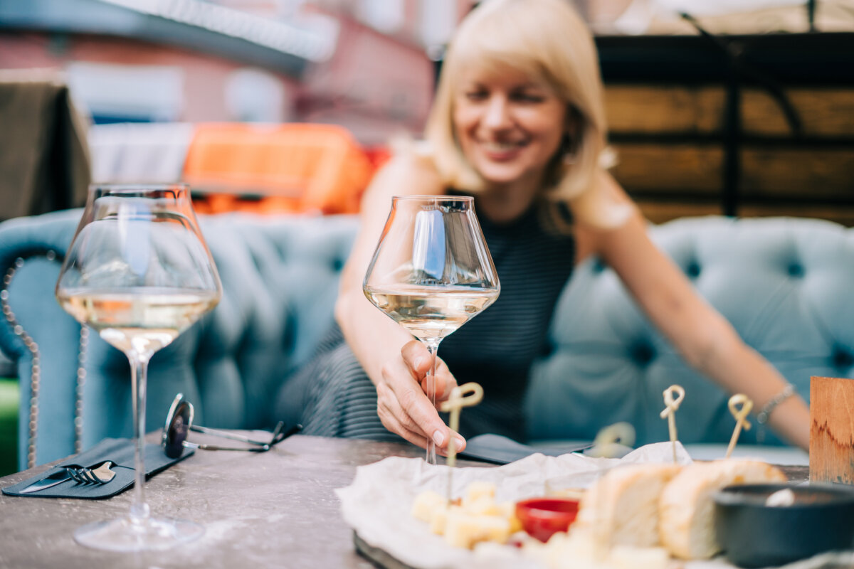 Grammar Guru: Compliment vs. Complement and Stationary vs. Stationery - 2 A person sits at an outdoor table reaching for a glass of white wine beside a cheese board, a scene that perfectly complements the relaxed atmosphere.