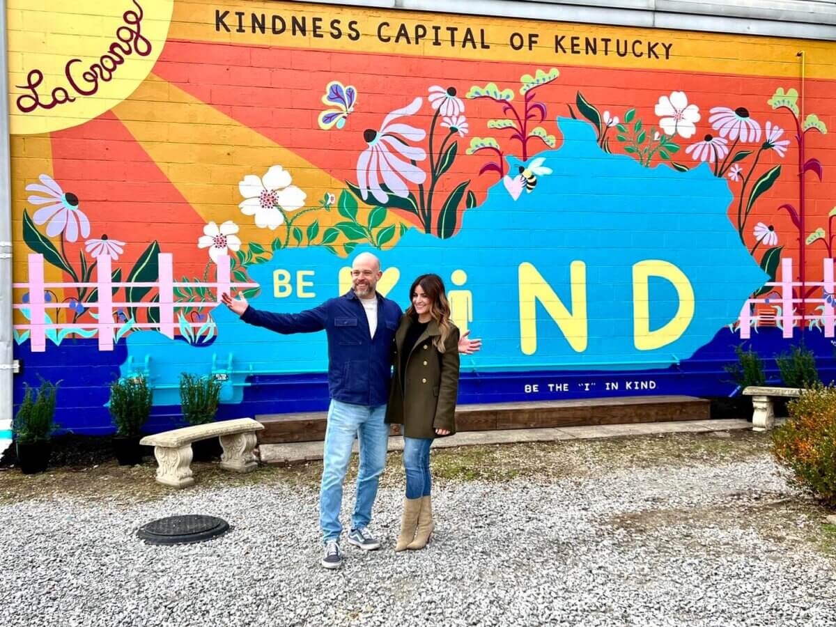 Our Favorite Historic Downtowns in the South to Explore - 3 Two people stand in front of a colorful mural in one of the South’s historic downtowns, reading “Kindness Capital of Kentucky” and “Be the ‘I’ in Kind,” with flowers and a bright sun design.