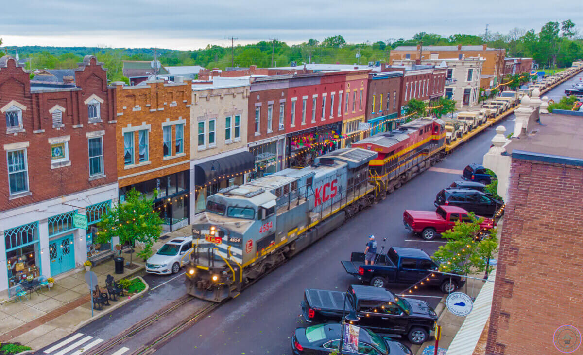 Our Favorite Historic Downtowns in the South to Explore - 2 A freight train travels down the main street of a small town in the South, passing parked cars and brick storefronts in its historic downtown on a cloudy day.