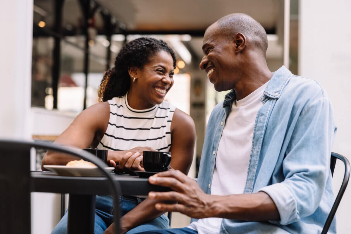 How Not to Date a Loser: Therapists Share the Red Flags You Shouldn't Ignore - 2 A couple laughing at an outdoor cafe table with coffee, unaware of the potential dating red flags in their toxic relationship.