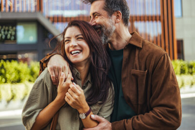 A man with his arm around a laughing woman standing outdoors, capturing a moment often discussed in relationship advice.