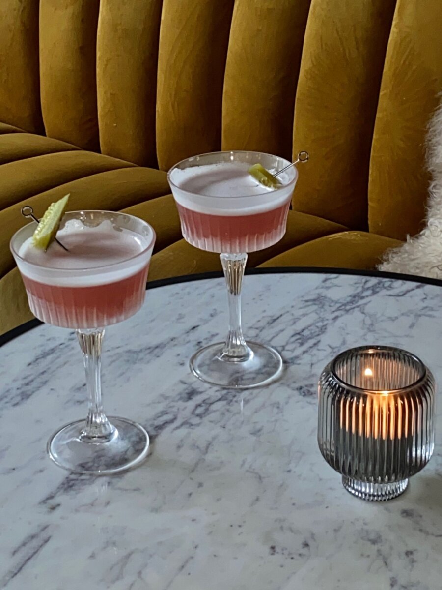 Two pink cocktails garnished with lime slices in fluted coupe glasses on a marble table with a lit candle, perfect for Louisville dining.