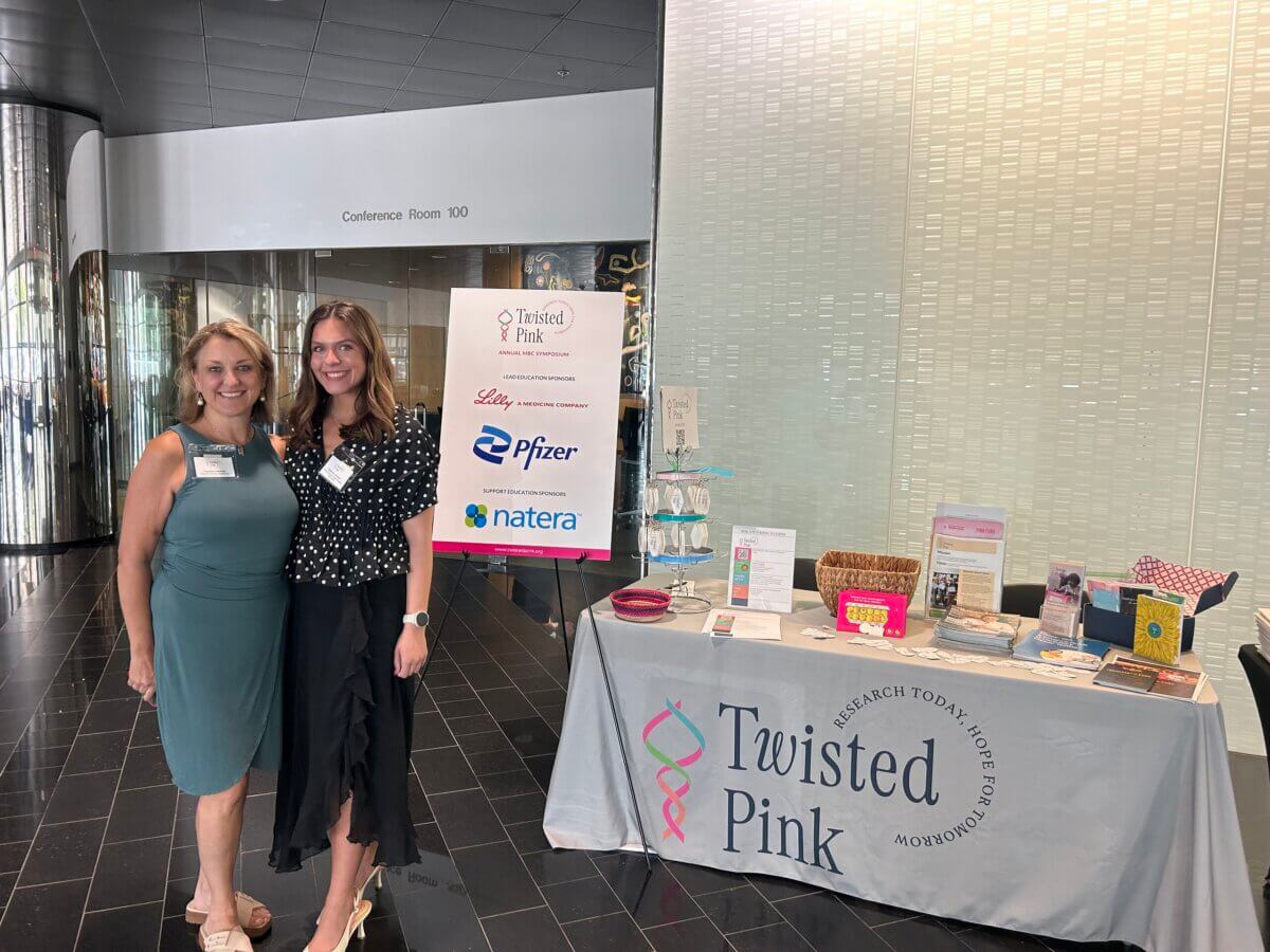 She Turned Her Darkest Moment Into a $2M Research Legacy. And She's Not Done Yet - 5 Two women stand by a Twisted Pink display table in a modern lobby, with informational materials and sponsor logos.