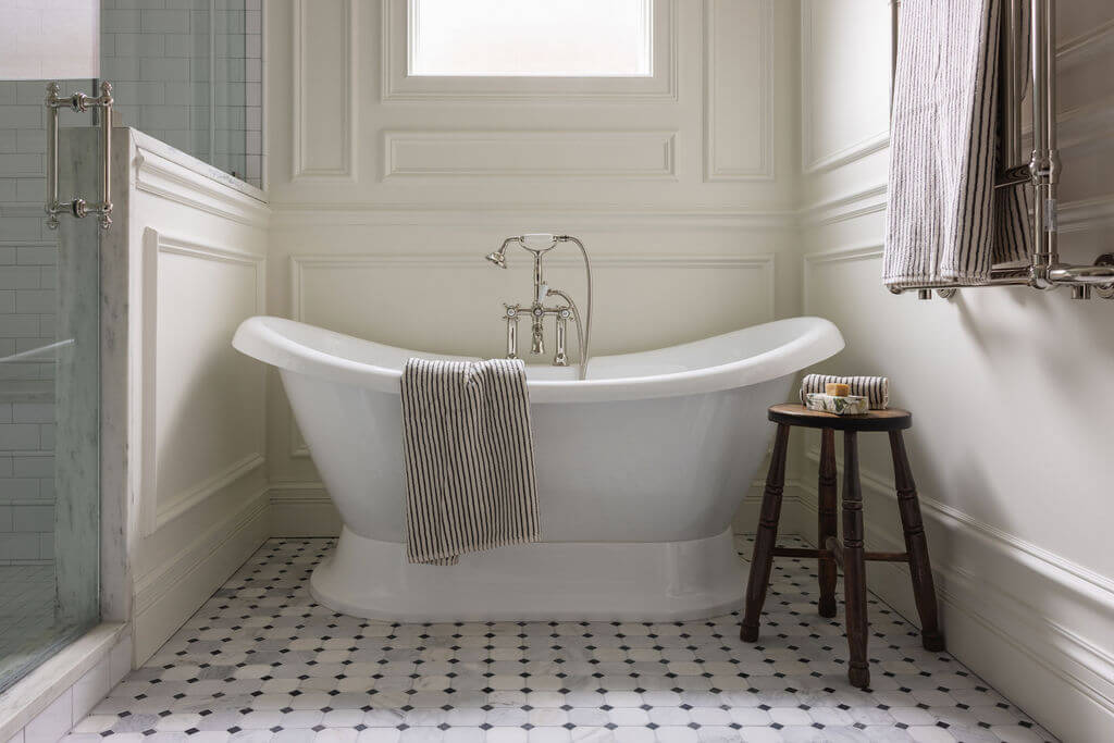 From ICU Nurse to Interior Designer: Meet Gretchen Rose of Kentucky Rose Designs - 4 A white pedestal bathtub centered in a Kentucky Rose Designs bathroom with marble mosaic tile flooring and a wooden stool.