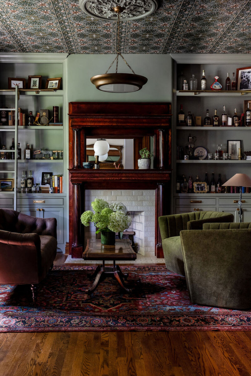 From ICU Nurse to Interior Designer: Meet Gretchen Rose of Kentucky Rose Designs - 7 A living room by interior designer Gretchen Rose featuring a fireplace with a wood mantel, built-in bookshelves, a floral patterned ceiling, and two armchairs facing a central coffee table.