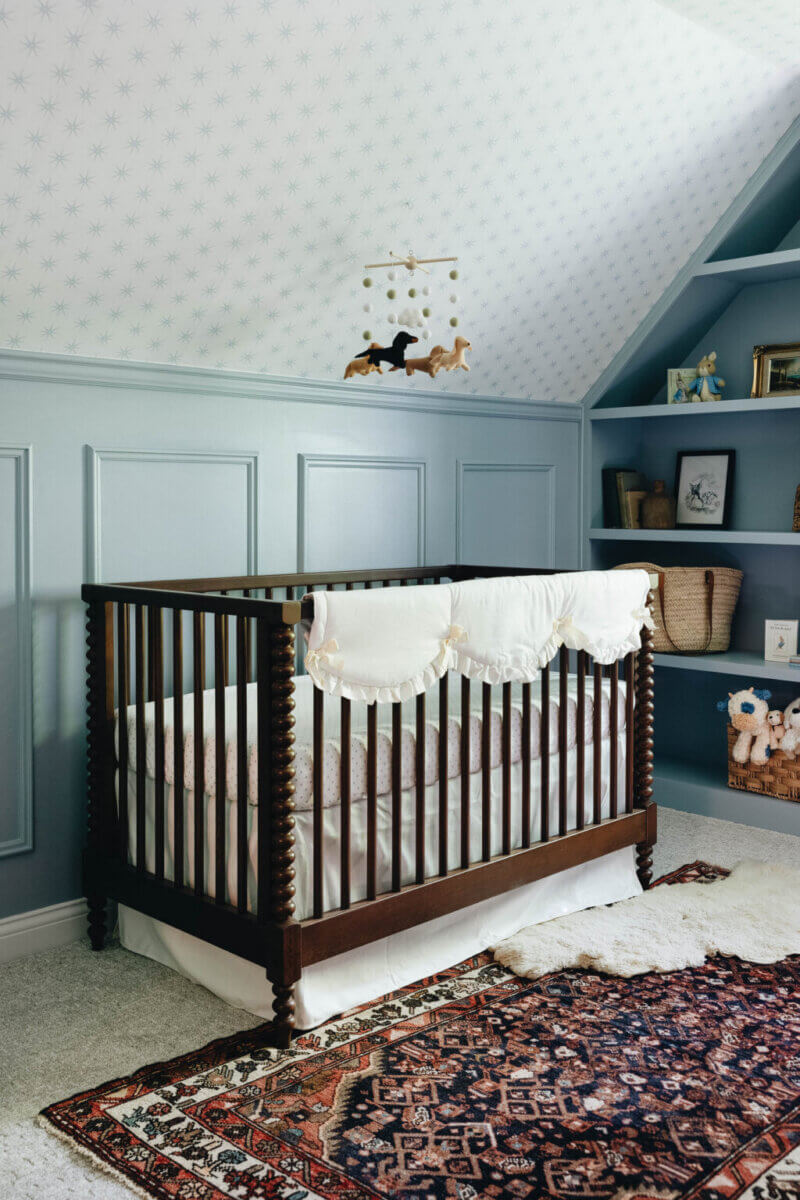 From ICU Nurse to Interior Designer: Meet Gretchen Rose of Kentucky Rose Designs - 12 A wooden spindle crib with a ruffled dust ruffle in a blue nursery designed by Kentucky Rose Designs, featuring built-in shelves and a patterned area rug.