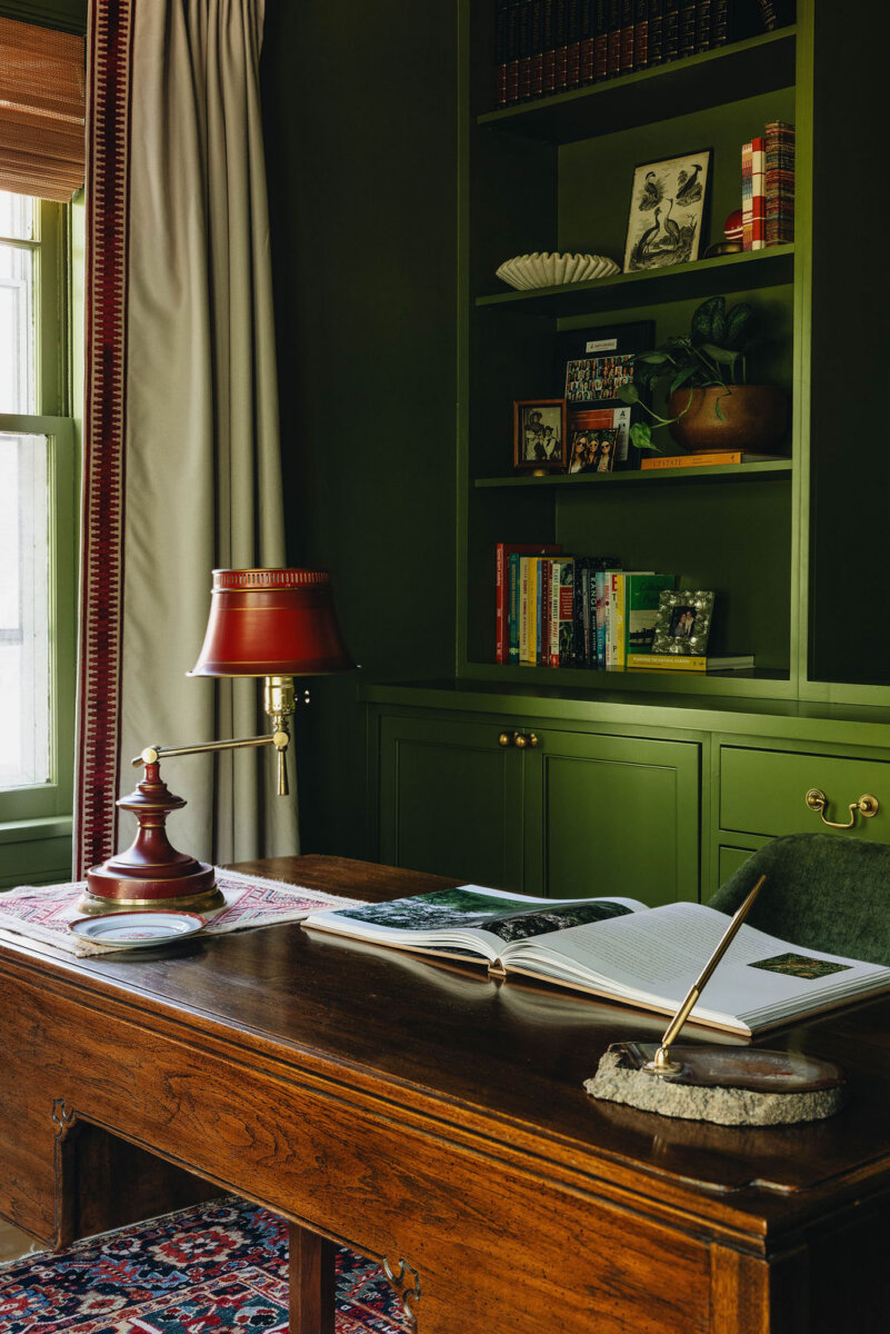 From ICU Nurse to Interior Designer: Meet Gretchen Rose of Kentucky Rose Designs - 15 A wooden desk featuring an open book, a lamp, and a pen holder sits in front of olive-green bookshelves, a space styled by Kentucky Rose Designs.