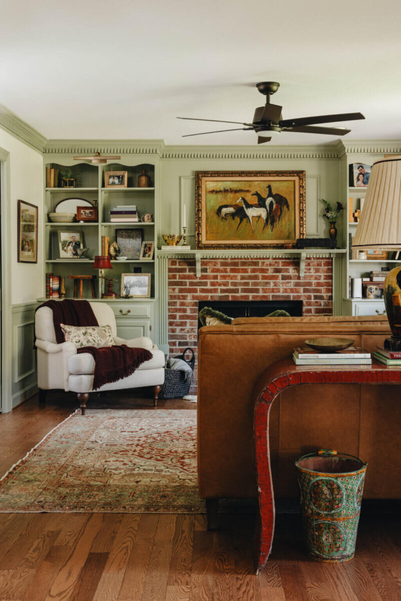 From ICU Nurse to Interior Designer: Meet Gretchen Rose of Kentucky Rose Designs - 19 Living room featuring Kentucky Rose Designs interior design with a brick fireplace, horse painting, built-in green shelves, an armchair, and a brown leather sofa.