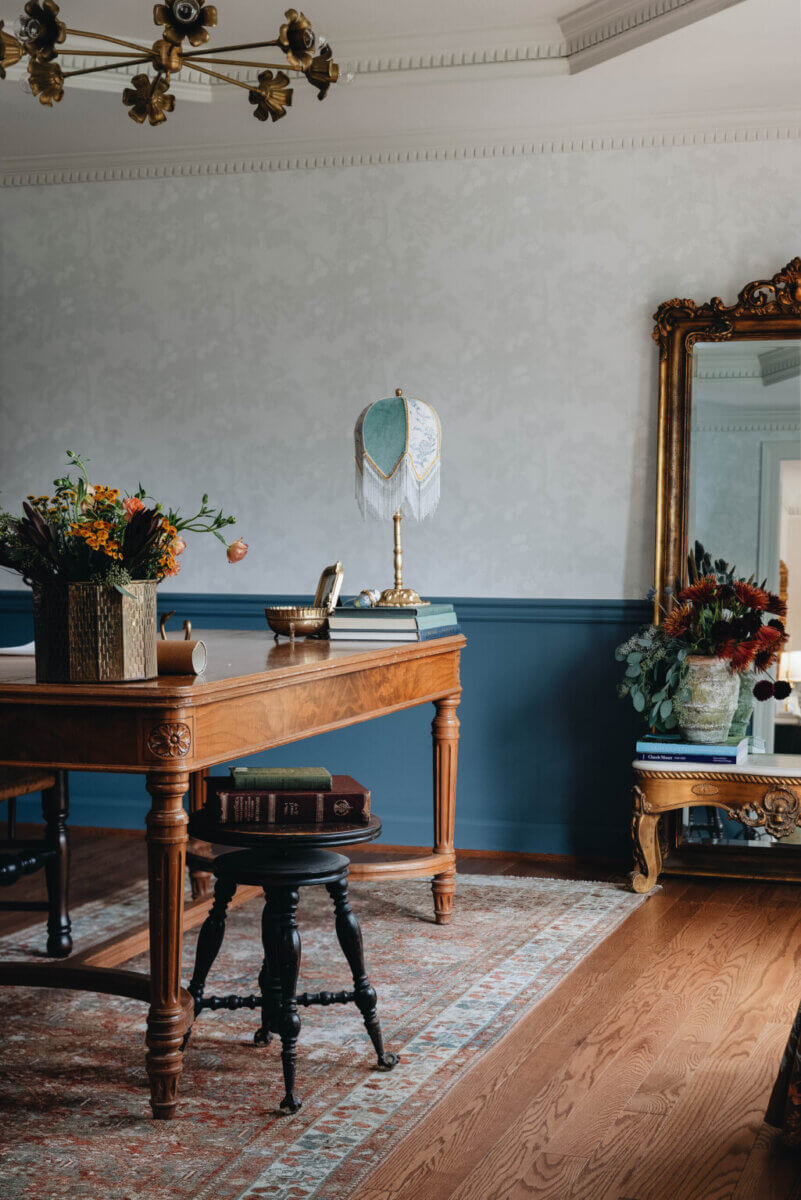 From ICU Nurse to Interior Designer: Meet Gretchen Rose of Kentucky Rose Designs - 18 A wooden desk by Kentucky Rose Designs sits in a room with a patterned rug, a fringed lamp, floral arrangements, and an ornate floor mirror.