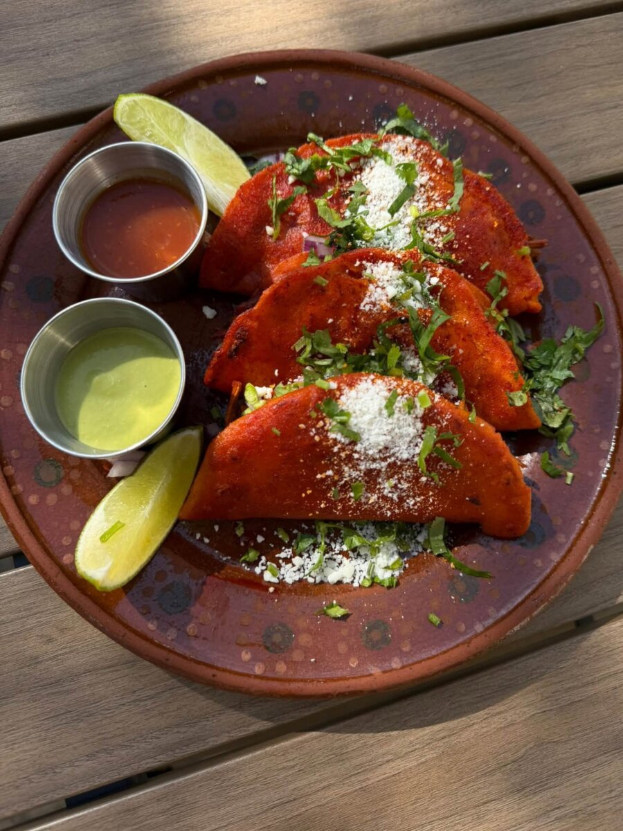Three birria tacos topped with cilantro and cotija cheese on a plate with lime wedges and salsa, a highlight of Louisville dining.