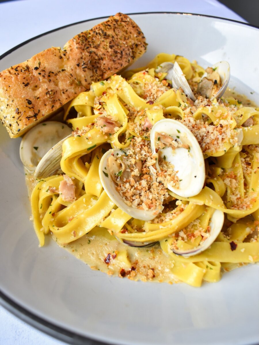 Linguine with clams in a light sauce topped with breadcrumbs, served with herb-crusted bread at a Louisville restaurant.