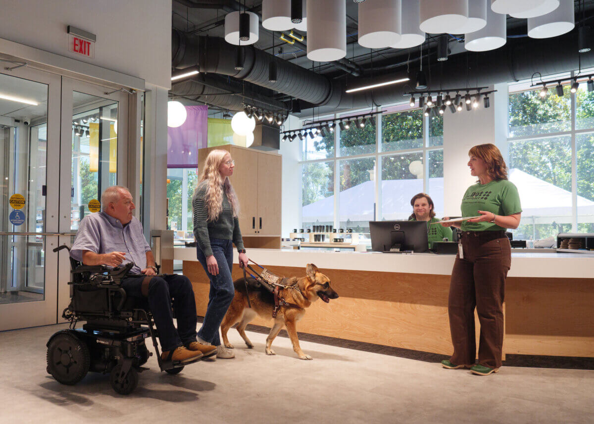 Stevie Wonder's Piano, Helen Keller's Desk & the Louisville Museum Where Every Guest Gets to Touch History - 3 A man in a power wheelchair and a woman with a German shepherd service dog speak to a staff member at The Dot Experience service desk.