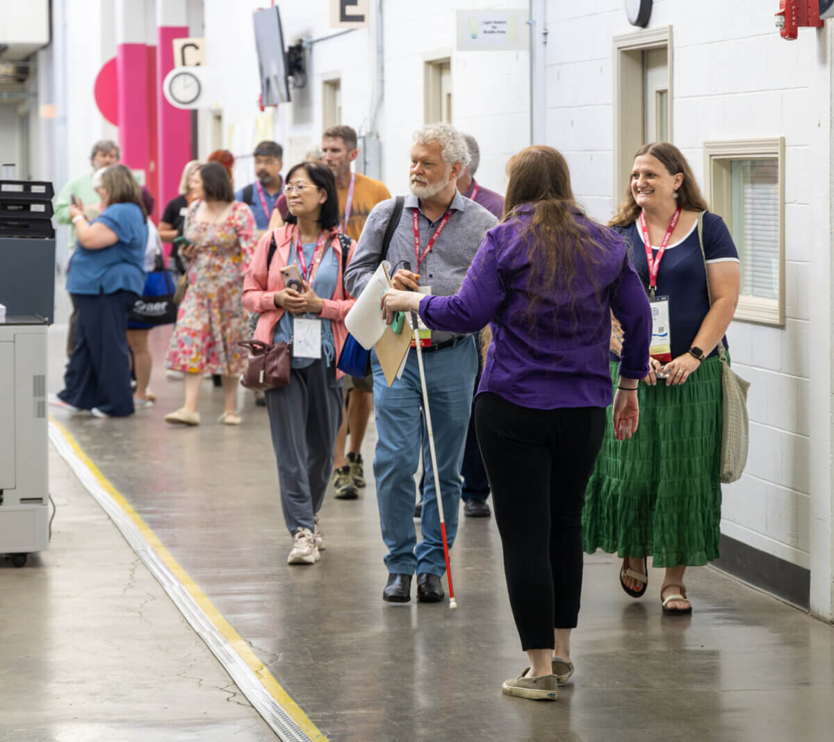 Stevie Wonder's Piano, Helen Keller's Desk & the Louisville Museum Where Every Guest Gets to Touch History - 7 A woman in a purple shirt uses a white cane to navigate a hallway during The Dot Experience as a group of people with conference lanyards walks behind her.
