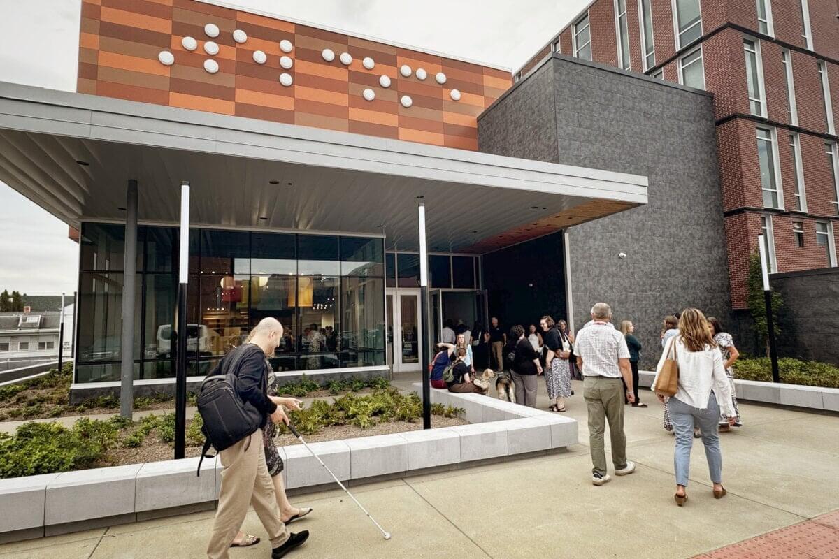 Stevie Wonder's Piano, Helen Keller's Desk & the Louisville Museum Where Every Guest Gets to Touch History - 2 People gather on a paved plaza outside a modern building with a facade featuring a braille pattern and a museum called Dot Experience.